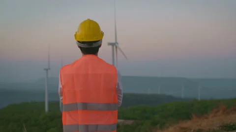 Back view of a man engineer is standing in a field  wearing a protective helm Stock Footage 149049261