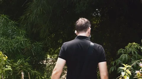 Back View of Man with Face Mask and Bag Walking Through Green Jungle Video stock 136835394