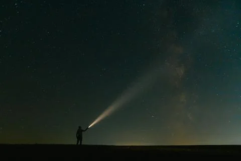 Back view of man with flashlight standing on green grassy field under beaut.. Stock Photos