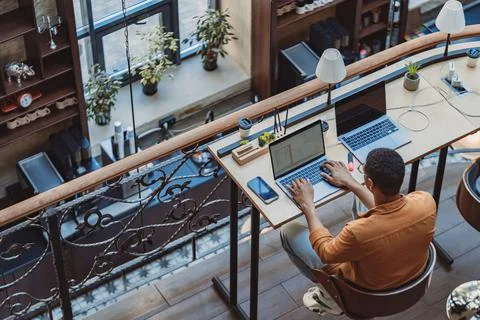 Back view of man freelancer working on laptop while sitting in modern coworking Stock Photos