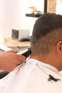 Back view of man getting short hair trimming at barber shop with clipper mach Stock Photos