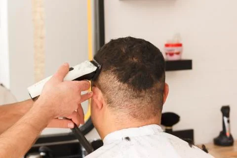 Back view of man getting short hair trimming at barber shop with clipper mach Stock Photos