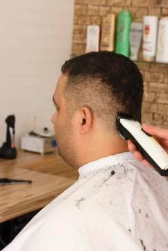 Back view of man getting short hair trimming at barber shop with clipper mach Stock Photos