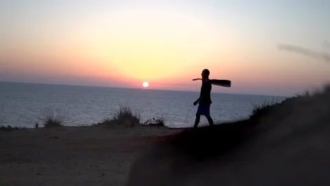 Back view of a man with guitar at sunset  walk along on rocks at the ocean beach Video stock 100185197