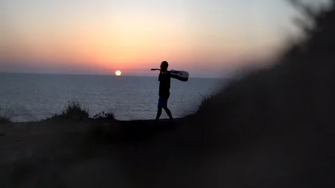 Back view of a man with guitar at sunset  walk along on rocks at the ocean beach Stock Footage 100185353