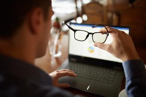 Back view of man hand holding eyeglasses in front of laptop screen with charts 库存照片