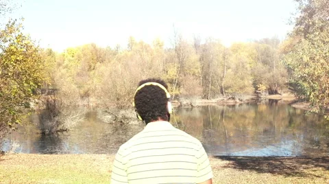 Back view of man with headphones listening to music by the lake Stock Footage 59555366
