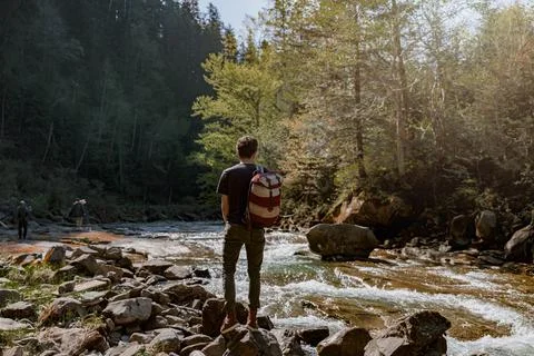 Back view on man hiker with backpack standing at river with rocks and enjoying Stock-Fotos