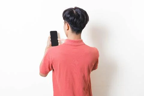 Back view of a man holding a smartphone against a plain background, showing.. Stock Photos