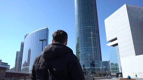 Back view of a man in a jacket admiring modern skyscrapers Stock Footage 194476215