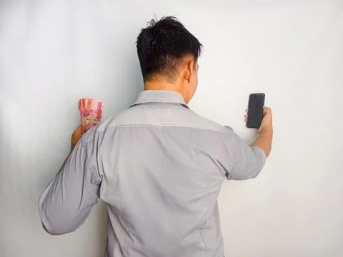 Back view of a man looking to the mobile phone and money that he hold Stock Photos