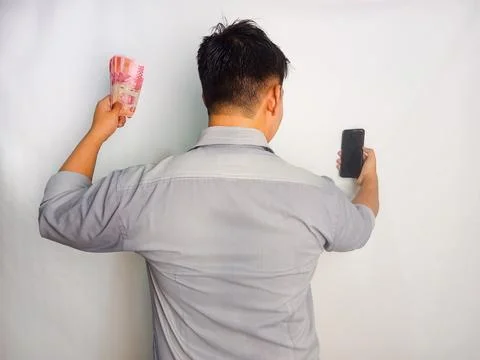 Back view of a man looking to the mobile phone and money that he hold Stock Photos