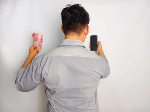 Back view of a man looking to the mobile phone and money that he hold Stock Photos