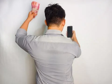 Back view of a man looking to the mobile phone and money that he hold Stock Photos