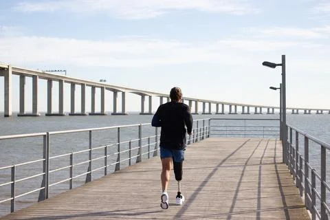 Back view of man with mechanical leg running on embankment Stock Photos