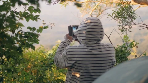 Back view of a man in peak wearing hooded jacket taking video with a smartphone. Stock Footage 118411904