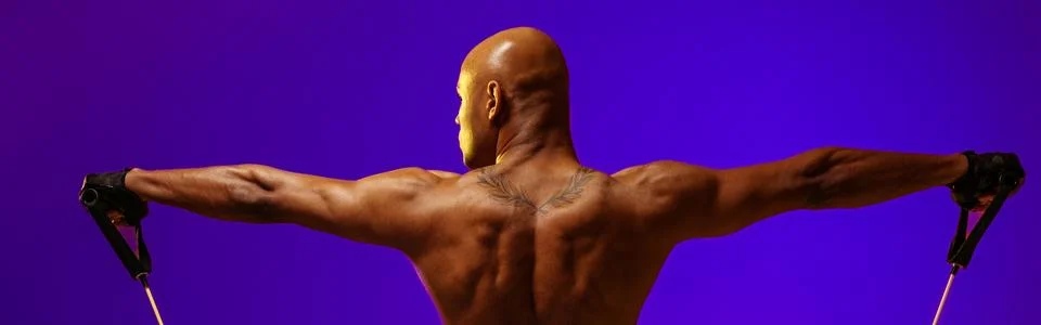 Back view of man performs exercises with expander on studio background. Strength Stock Photos