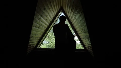 A back view of a man putting on a jacket in front of a triangular window in a Видео 96307126