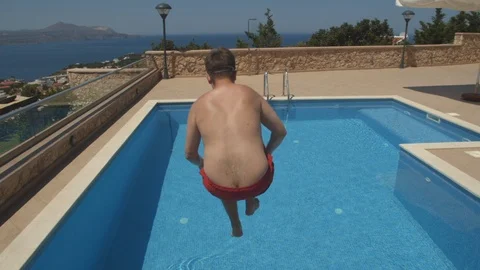 Back view of man in red swim shorts running and jumping to the swimming pool. Video stock 113971736