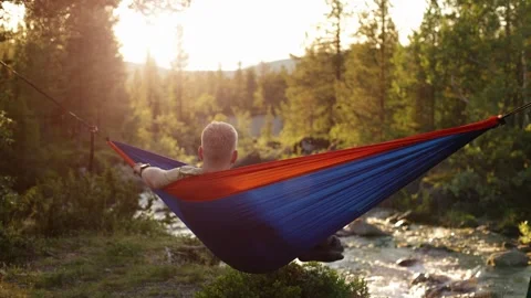 Back view of a man resting in a hammock, admiring the view of the river Stock Footage 249437956