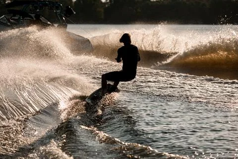 Back view of man riding wakeboard behind motor boat on splashing river waves 스톡 사진