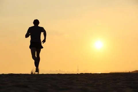 Back view of a man running on the beach at sunset Stock Photos