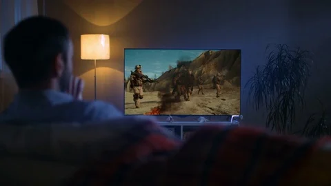 Back View of a Man Sitting on a Couch Watching War Movie on His  TV Video stock 72523137