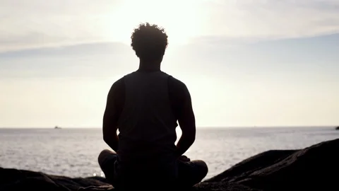 Back view of man sitting in lotus position and meditating at sunset Stock Footage 123490023
