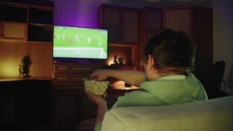 Back view of man sitting on sofa watching football match on TV in room 库存影片 314396104