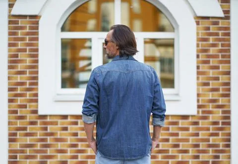 Back view of a man standing alone looking sideways at old town building while Stock Photos