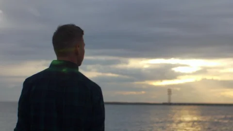Back view of a man standing on the pier, enjoying sunset over sea. SLOW MO Stock Footage 97450256