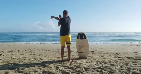 Back view of man stretching his body warm up before surfing against ocean. Video stock 213978209