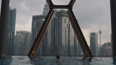 Back view of man swim and relax on the edge of the roof top swimming pool in Video stock 231279697