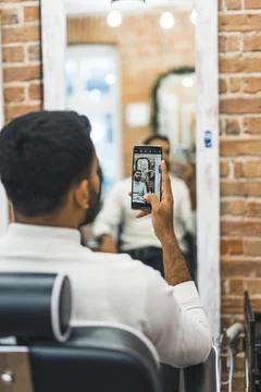 Back view of a man taking a mirror selfie at the barbershop, vertical shot Stock Photos