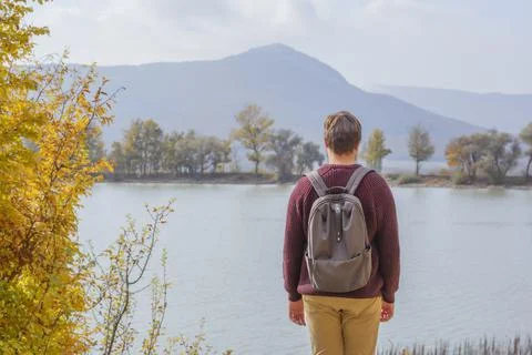 Back view man tourist with backpack in sweaters near the lake in the forest in Stock Photos