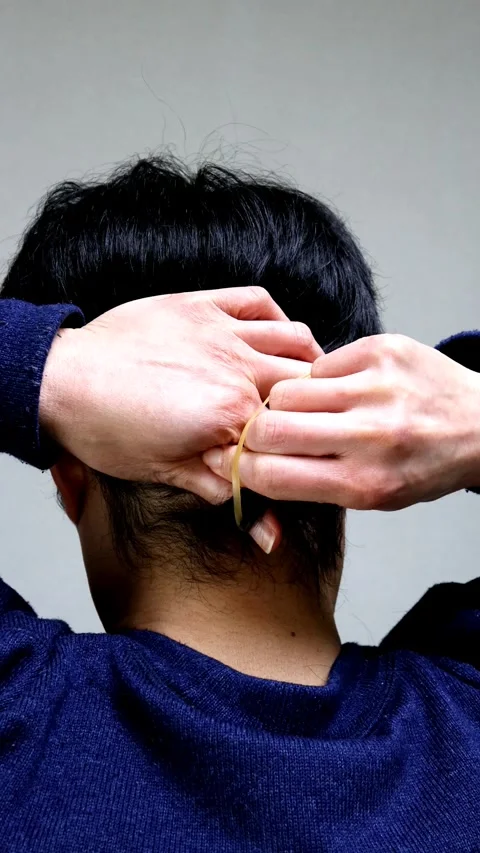The back view of a man tying his hair up for the first time in his life. Video stock 336226642