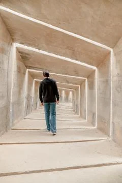 Back view of man walking alone in tunnel corridor. Urban underground lonely w Stock Photos