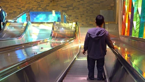 Back view of man walking down electric stairs beside still man witch backpack Stock Footage 87346653