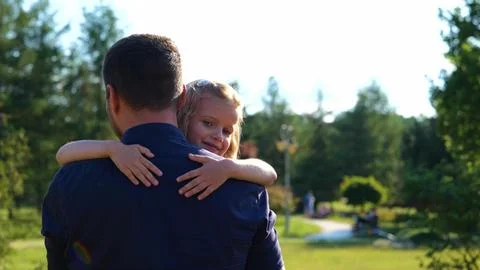 Back view of man walking in nature holding his little daughter in arms. Pretty Stock Photos