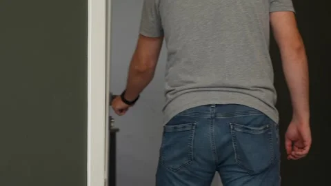Back view of a man wearing a grey T-shirt and jeans as he opens a white doo.. Video stock 321285404