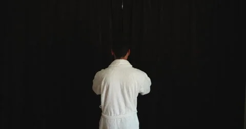Back view of a man in white bathrobe going to the window to open the curtains in Video stock 156968778