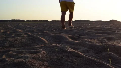 A back view of a man in yellow shorts walking slowly across the sandy terrain Video stock 158191414