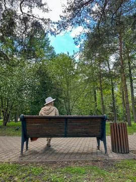 Back view A middle-aged blonde girl is sitting in a park on a bench and loo.. Stock Photos