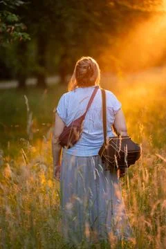 Back view of middle aged female photographer standing in meadow at sunset w.. Stock Photos