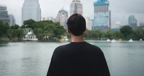 Back view millennial lonely man standing looking at lake in the park overlooking Stock Footage 251700953