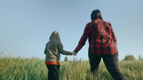 Back view mom and son walk holding hands walk through the grass in the field. Stock Footage 244492975