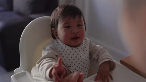 Back view of mom feeding her baby. Toddler is sitting on a high chair and eating Stock Footage 244635590