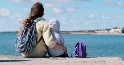 Back view Mother and child sit on the waterfront and look at the water Video stock 164856026