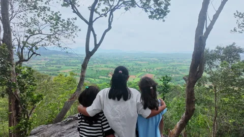 Back view of mother and daughters embracing on windy mountain cliff Video stock 343197521