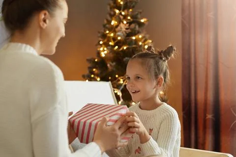 Back view of mother giving gift for her loving child on Xmas Day, daughter .. Stock Photos